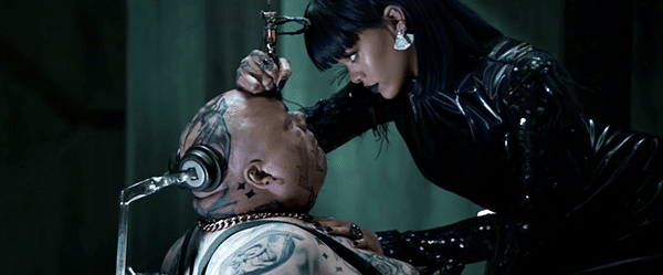 Still dressed in black, Rihanna tattooes a guy (who appears to be unable to move) right on the forehead.