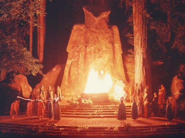 "The Cremnation of Care" at the Bohemian Grove. The ceremony involves the poling of a small boat across a lake containing an effigy of Care (“Dull Care”). Dark, hooded individuals receive the effigy from the ferryman which is placed on an altar and, at the end of the ceremony, is set on fire.