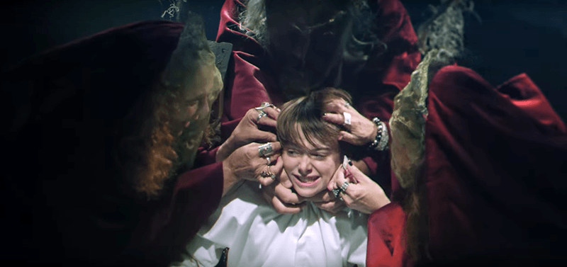 A bunch of witches attach wires to the boy's head.