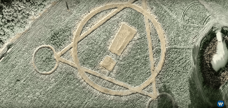 As the camera pans out, we see a crop circle shaped in something resembling an alchemical symbol. The exclamation point is taken from the band's name, indicating that their the one's behind this. 