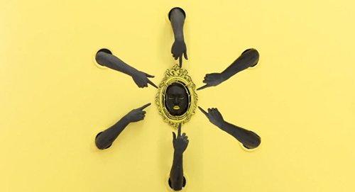 The black face is surrounded by six arms pointing towards it.