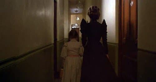 The head nurse, dressed in a creepy black dress, walks Dorothy to her room. 