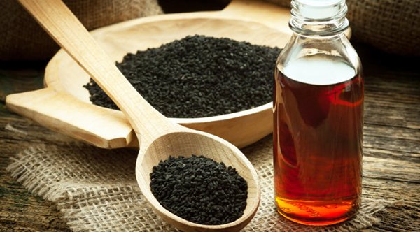 Nigella sativa (Black cumin) on wooden spoon and essential oil. Real oil from nigella looks like dark honey